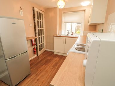 A kitchen with a refrigerator microwave electric stove sink window and wooden floor at Magpie Cottage in Morpeth