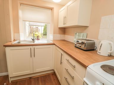 A kitchen with a sink below a window a toaster and electric kettle on the counter at Magpie Cottage in Morpeth