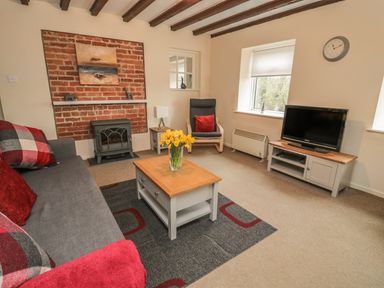 A living room with a gray sofa a coffee table with flowers a fireplace and a TV at Magpie Cottage in Morpeth