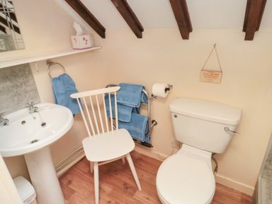 A bathroom with a toilet sink white chair blue towels and wooden beams on the ceiling at Magpie Cottage Morpeth