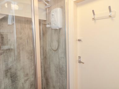 A shower area with an electric shower unit and a door with hooks at Magpie Cottage in Morpeth