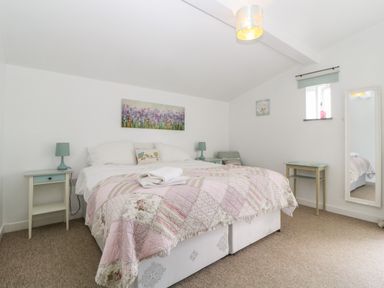 A bedroom with a double bed bedside tables lamps a chair a wall mirror and two paintings at Owl Barn in Tavistock