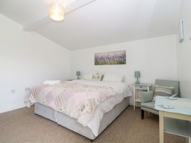 A bedroom with a double bed two bedside tables lamps an armchair and a small table at Owl Barn in Tavistock