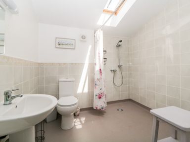 A bathroom with a sink, toilet, walk-in shower with floral curtain, skylight, and small stool at Owl Barn in Tavistock