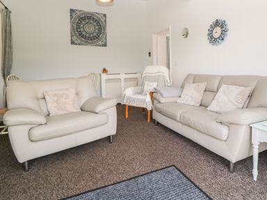 A living room with two beige sofas a chair a wall clock and a painting at Owl Barn in Tavistock