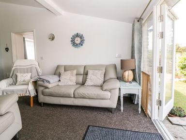 A living room with a sofa armchair side table lamp and open patio doors at Owl Barn in Tavistock