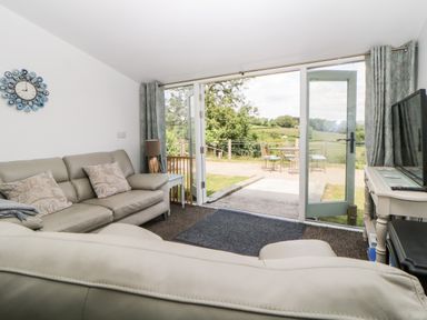 A living room with leather sofas a TV and glass doors opening to a patio at Owl Barn in Tavistock
