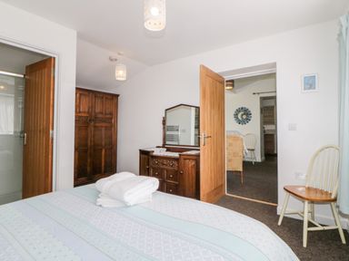 A bedroom with a bed folded towels a wooden dresser and mirror an open wooden door and a chair at Owl Barn in Tavistock