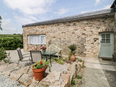 An outdoor patio area with a stone wall house a glass table with chairs and potted plants at Owl Barn in Tavistock