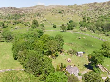 A house surrounded by trees and fields with hills in the background at Cae Lleci Llanfachreth near Dolgellau