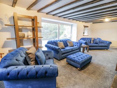 A living room with blue sofas a matching ottoman wooden shelves and exposed ceiling beams at Cae Lleci Llanfachreth near Dolgellau
