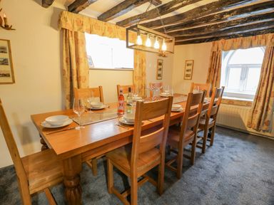 A dining room with a wooden table set for six with wine bottles under exposed beam ceiling at Cae Lleci in Llanfachreth near Dolgellau
