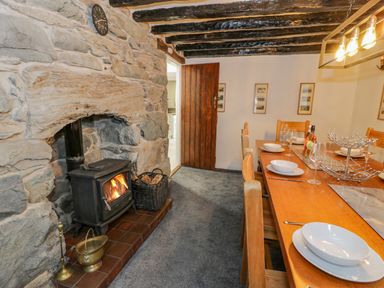 A dining room with a wooden table set for six people near a stone wall with a wood burning stove at Cae Lleci in Llanfachreth near Dolgellau