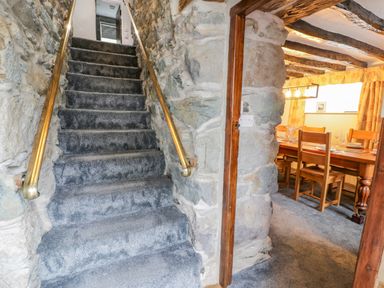 Stone walls with carpeted stairs and a wooden dining table with chairs in a room at Cae Lleci in Llanfachreth near Dolgellau