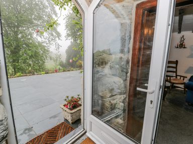 An open door leading to a tiled patio with a stone planter and plants at Cae Lleci in Llanfachreth near Dolgellau