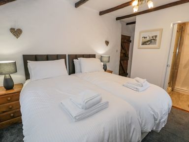 A bedroom with two single beds side by side each with white bedding and towels on top two bedside tables with lamps wooden door and a framed picture on the wall at Cae Lleci in Llanfachreth near Dolgellau