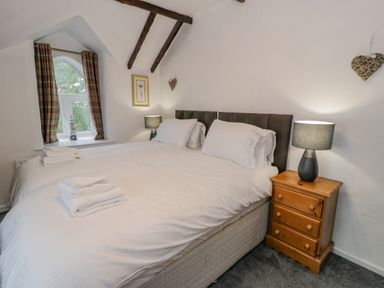 A bedroom with two beds side by side a wooden nightstand with a lamp and a window with curtains at Cae Lleci in Llanfachreth near Dolgellau