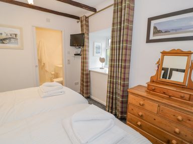 A bedroom with two beds a wooden dresser with mirror a wall-mounted TV and a window with plaid curtains at Cae Lleci in Llanfachreth near Dolgellau