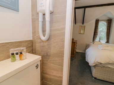 A bathroom corner with toiletries and a wall-mounted hair dryer next to a bedroom with a bed and window with curtains at Cae Lleci in Llanfachreth near Dolgellau