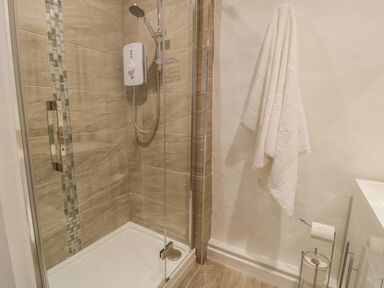 A bathroom with a walk-in shower a white towel on the wall and toilet paper rolls at Cae Lleci in Llanfachreth near Dolgellau