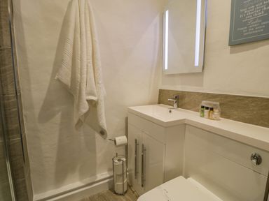 A bathroom with a white sink cabinet a towel hanging on the wall and toiletries on the counter at Cae Lleci Llanfachreth near Dolgellau