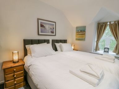 A bedroom with two single beds, wooden bedside tables with lamps, paintings on the walls, and a window with curtains at Cae Lleci Llanfachreth near Dolgellau
