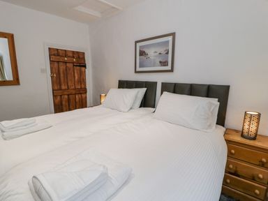 A bedroom with two single beds bedside lamp wooden chest of drawers and a wooden door at Cae Lleci Llanfachreth near Dolgellau