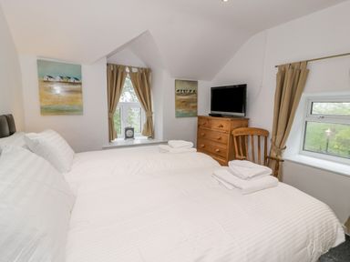 A bedroom with a bed folded towels wooden chest of drawers a television and windows with curtains at Cae Lleci Llanfachreth near Dolgellau