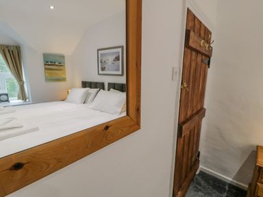 A wooden door and a mirror reflecting a bed with pillows and wall paintings at Cae Lleci in Llanfachreth near Dolgellau