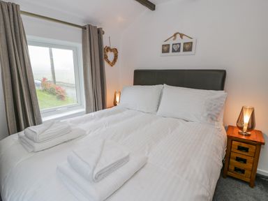 A bedroom with a large bed white linens bedside tables and a window with curtains at Cae Lleci in Llanfachreth near Dolgellau