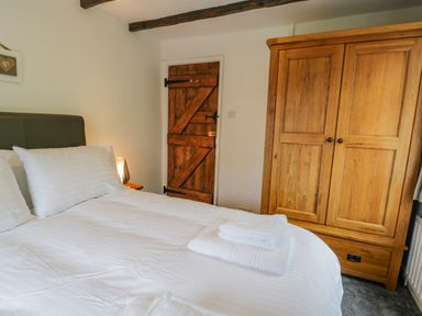 A bedroom with a double bed white linens folded towels on bed wooden wardrobe and wooden door at Cae Lleci Llanfachreth near Dolgellau