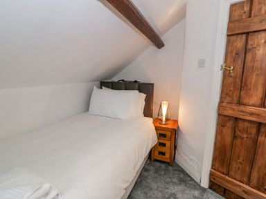 A single bed with white bedding and pillows next to a wooden nightstand with a lamp in a small room with a slanted ceiling and a wooden door at Cae Lleci Llanfachreth near Dolgellau