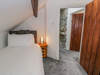 A bedroom with a single bed a wooden bedside table with a lamp and an open door showing a stone wall at Cae Lleci in Llanfachreth near Dolgellau