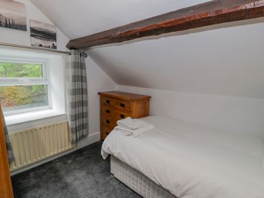 A small bedroom with a single bed next to a wooden chest of drawers and a window with plaid curtains at Cae Lleci Llanfachreth near Dolgellau