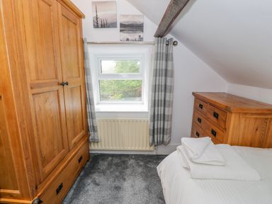 A bedroom with wooden wardrobe and chest of drawers a window with striped curtains and folded towels on the bed at Cae Lleci Llanfachreth near Dolgellau