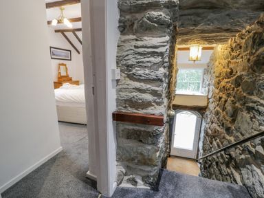 A stone-walled staircase leading to a white door and a bedroom with wooden furniture and exposed beams at Cae Lleci in Llanfachreth near Dolgellau