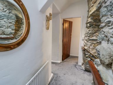 A hallway with stone walls a wooden door a circular mirror and two owl wall decorations at Cae Lleci Llanfachreth near Dolgellau