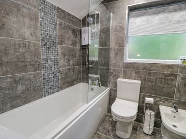 A bathroom with a bathtub shower combination a toilet a sink and a window with a blind at Cae Lleci in Llanfachreth near Dolgellau