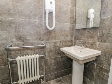 A bathroom corner with a white pedestal sink a chrome towel radiator and a wall-mounted hairdryer at Cae Lleci in Llanfachreth near Dolgellau