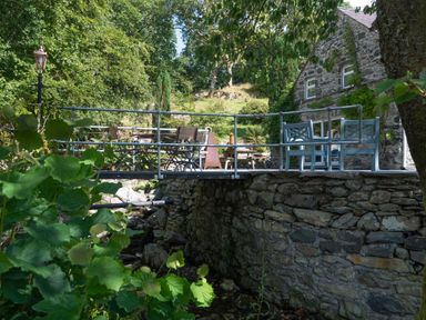 An outdoor stone patio with metal railings tables and chairs next to a stone building at Cae Lleci in Llanfachreth near Dolgellau