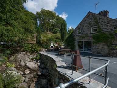 A stone house with a patio and outdoor furniture next to a rocky stream at Cae Lleci in Llanfachreth near Dolgellau