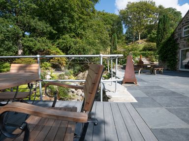 An outdoor patio area with wooden chairs a metal railing stone steps and greenery at Cae Lleci in Llanfachreth near Dolgellau