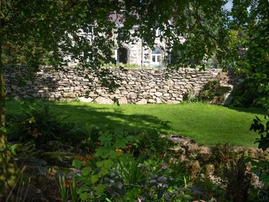 A garden with a stone wall and green grass in front of a stone house at Cae Lleci in Llanfachreth near Dolgellau