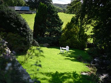 A garden area with green grass a white table and two chairs surrounded by trees and bushes at Cae Lleci Llanfachreth near Dolgellau