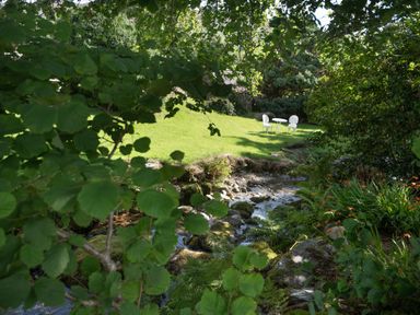 A garden with green grass a small white table with two white chairs near a rocky stream at Cae Lleci Llanfachreth near Dolgellau