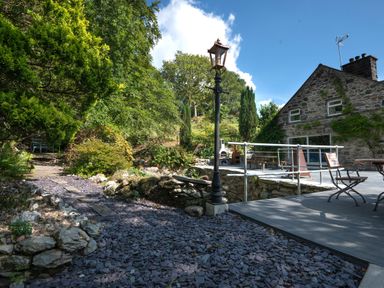 An outdoor area with stone pathway wooden chairs stone house and metal lamppost at Cae Lleci Llanfachreth near Dolgellau