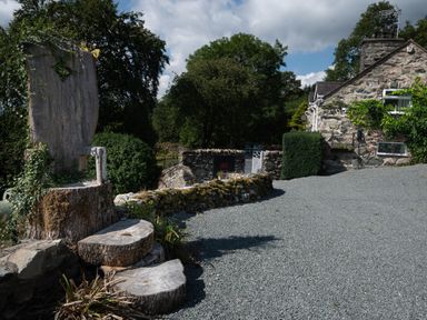 A stone house with gravel driveway and stone wall with wooden carved chair in the garden at Cae Lleci Llanfachreth near Dolgellau