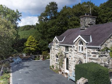 Stone cottage with slate roof and paved patio surrounded by trees at Cae Lleci in Llanfachreth near Dolgellau