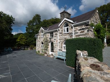 A stone house with white framed windows and a slate tiled patio with blue benches at Cae Lleci in Llanfachreth near Dolgellau