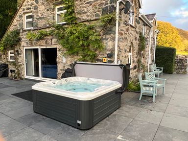 An outdoor hot tub with chairs on a patio outside a stone house at Cae Lleci Llanfachreth near Dolgellau